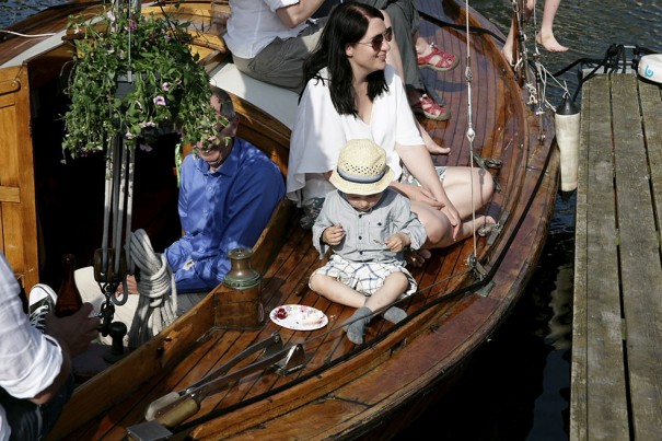 Festligt foto på träbåt vid brygga med barn som äter tårta.